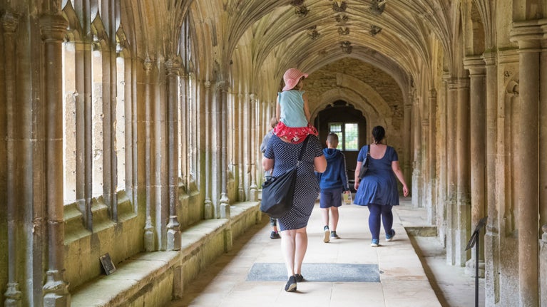 Family in summer clothes walking through the cloister at Lacock Abbey